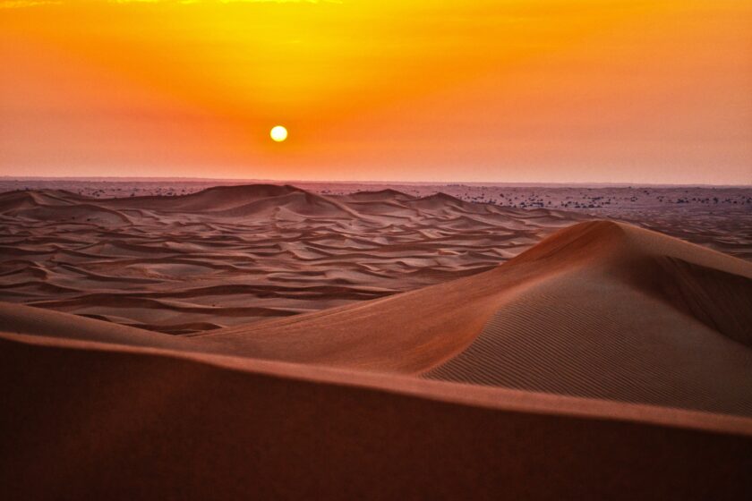 A sunset over the desert with sand dunes.